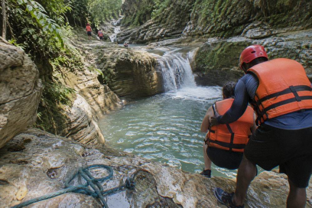 A guide in a helmet steadying a visitor at the edge of a rock pool