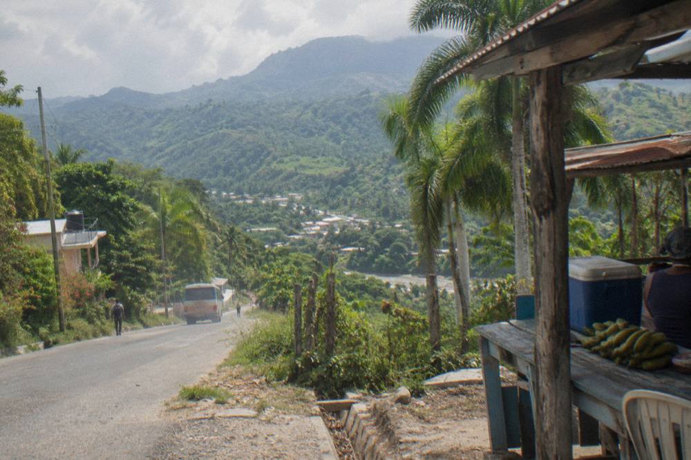 Winding rural road through green hills toward a small town in the Dominican countryside