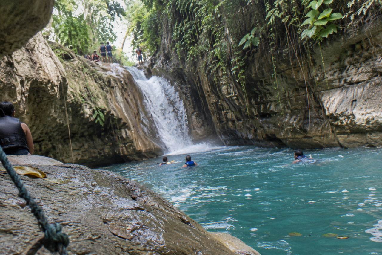 Turquoise waterfall pool in a narrow forested canyon with limestone walls