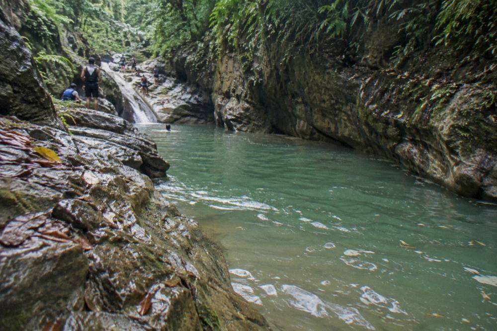 A river pool at the base of a rock canyon, the water tinted green after rain