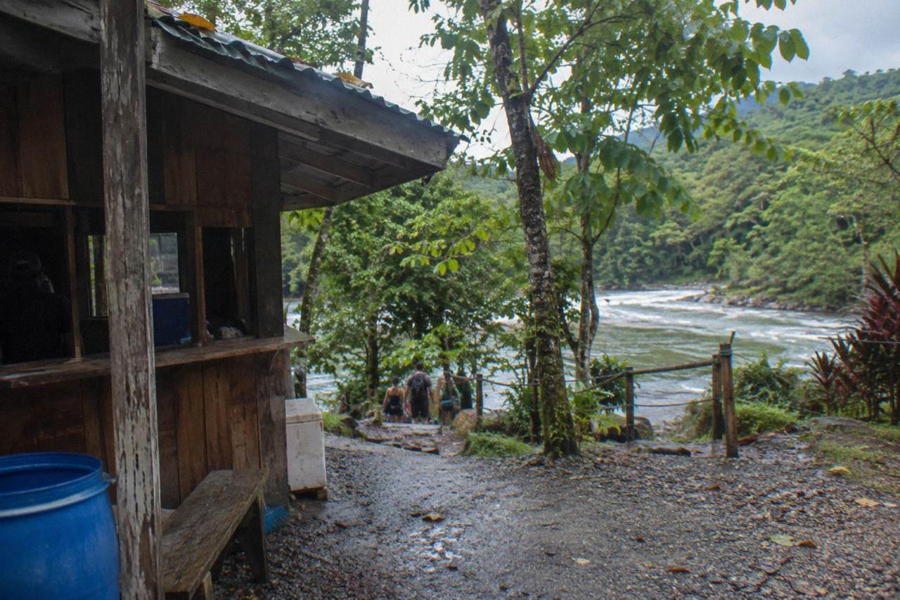 A small wooden ticket booth beside a forest trail with a river visible behind it