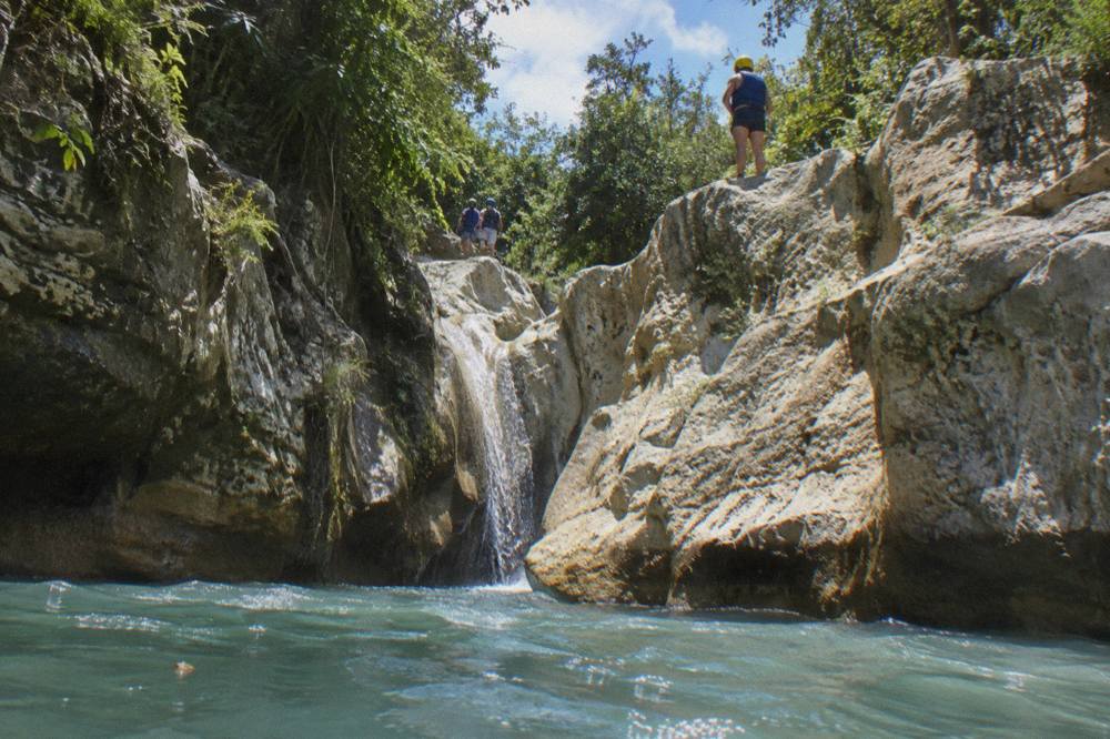 Waterfall sliding into a clear canyon pool framed by limestone walls and green forest