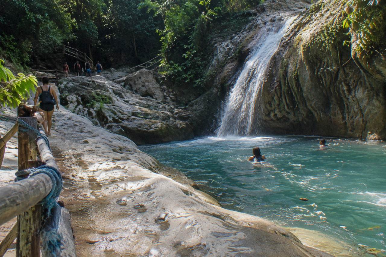 Turquoise pool at the bottom of a jungle waterfall with rock walls rising on both sides