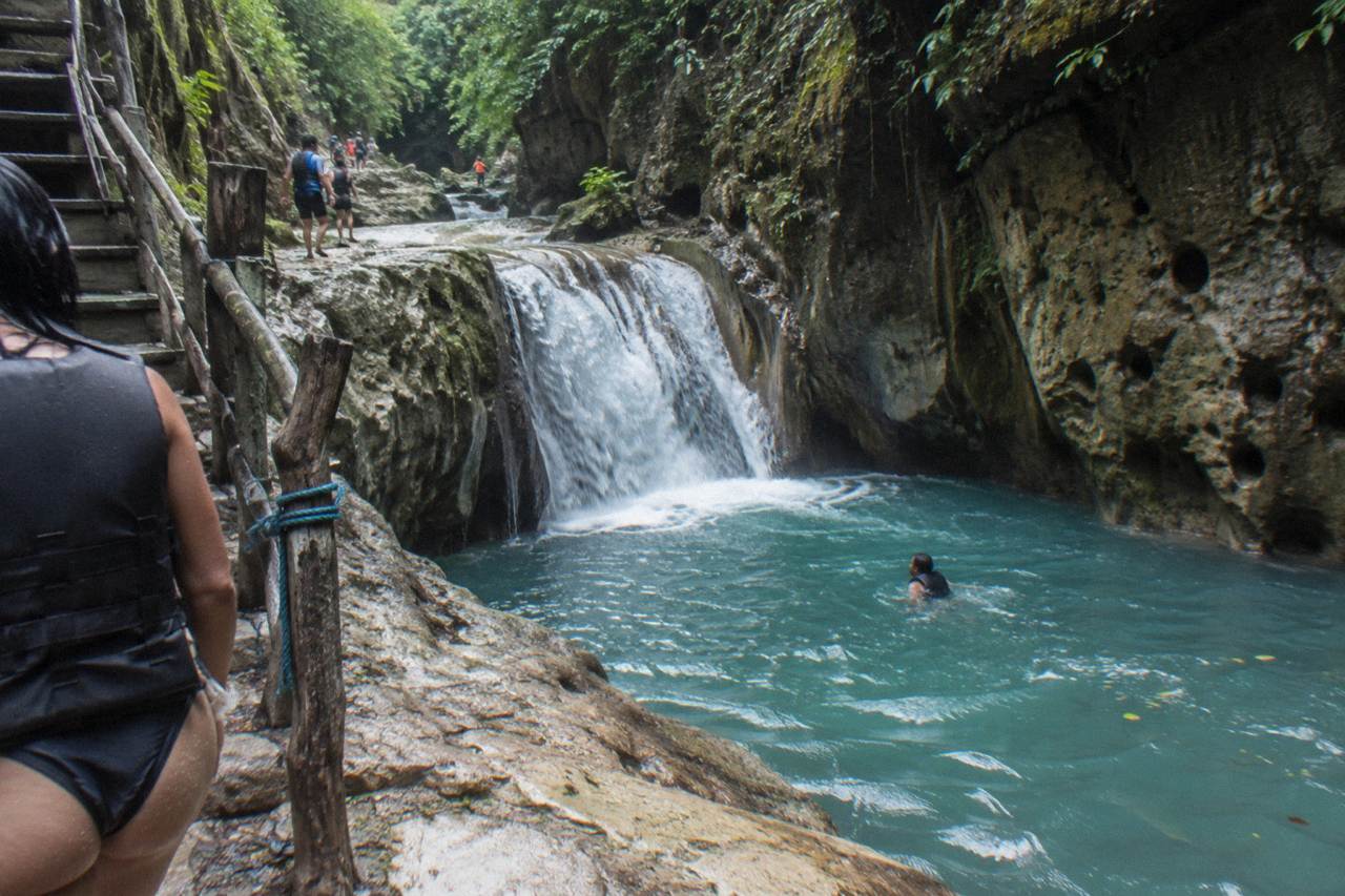 A narrow canyon river dropping into a turquoise pool surrounded by rocky walls and green forest