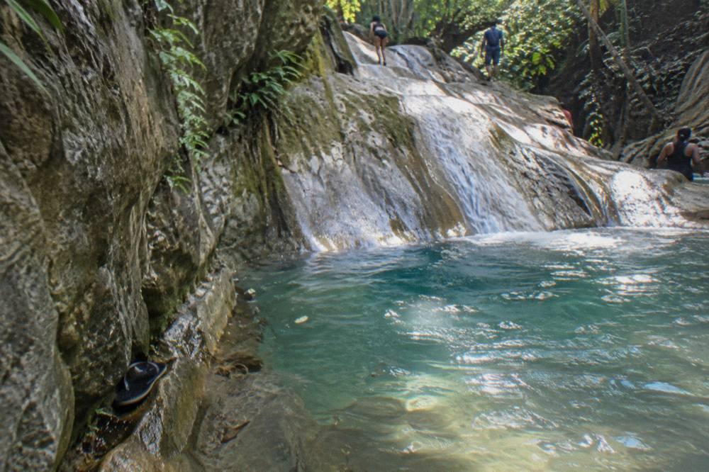A shallow turquoise pool at the base of a rock slide inside a forested canyon