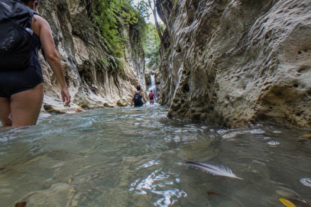 A narrow canyon passage with clear water and smooth rock walls rising on both sides
