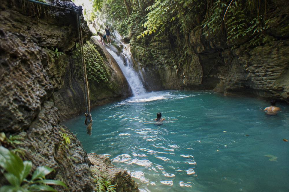 Turquoise waterfall pool in a narrow forest canyon with rocky walls