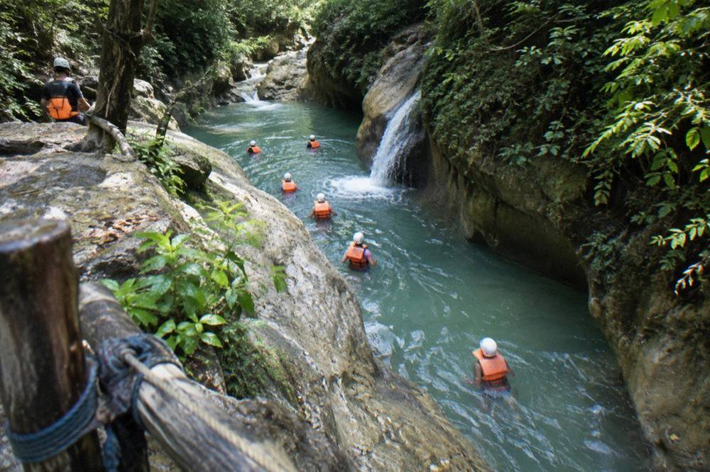 Guided group in helmets and life vests wading through a jungle river canyon