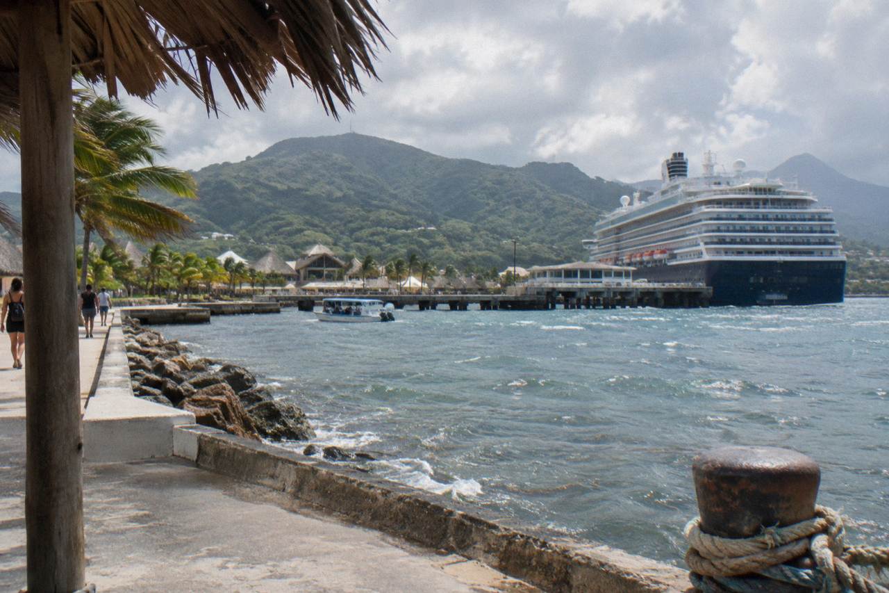 Cruise ship docked at a tropical port with green hills rising behind the terminal
