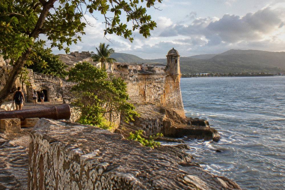 Historic stone fortress walls overlooking a Caribbean harbor in late afternoon light