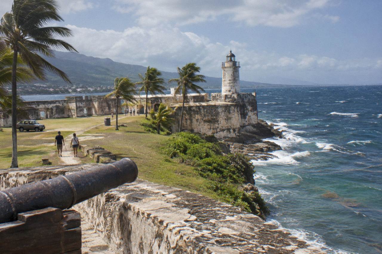Pale stone walls of Fortaleza San Felipe beside the sea in Puerto Plata, with lighthouse, lawn and palms