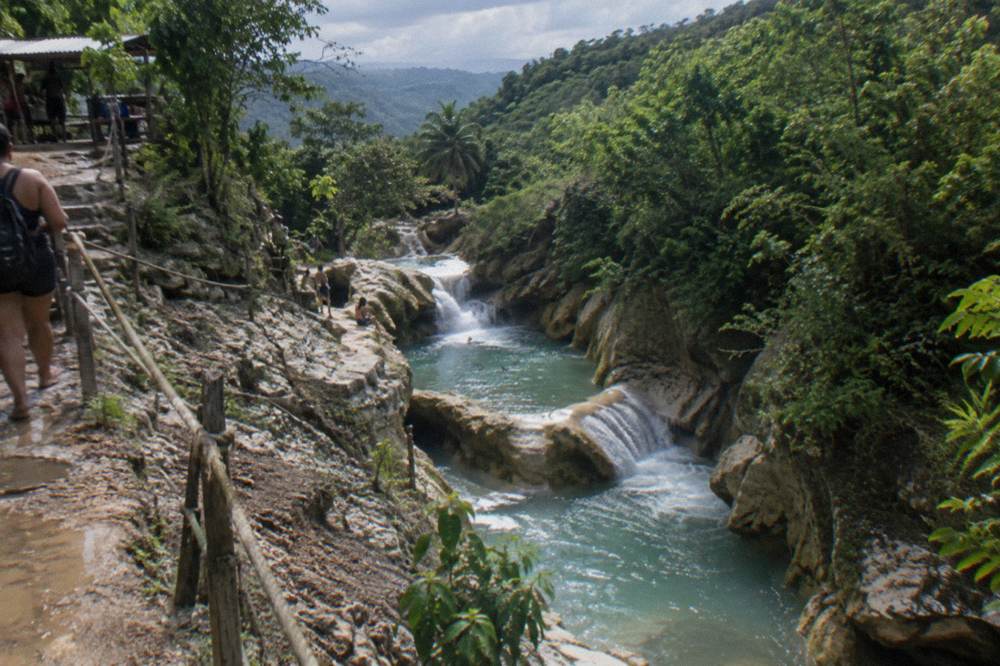 Tropical river valley with layered rock ledges and dense green vegetation under a blue sky