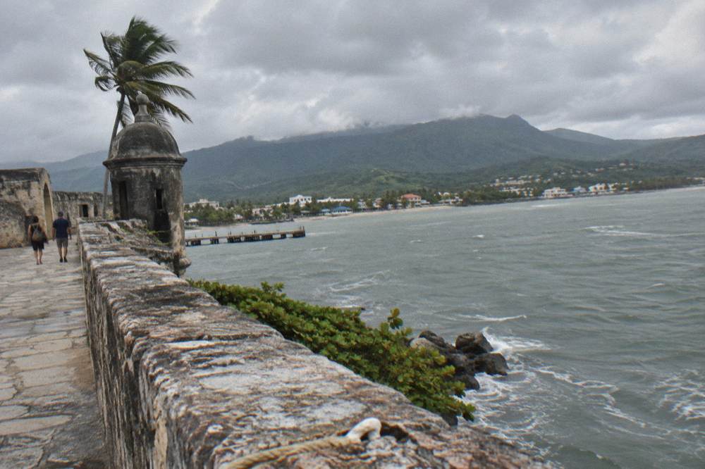 A colonial stone fortress wall overlooking a harbor with green hills behind