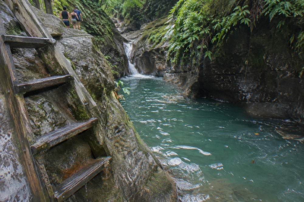 Wooden ladder descending beside a rock face into a clear pool below