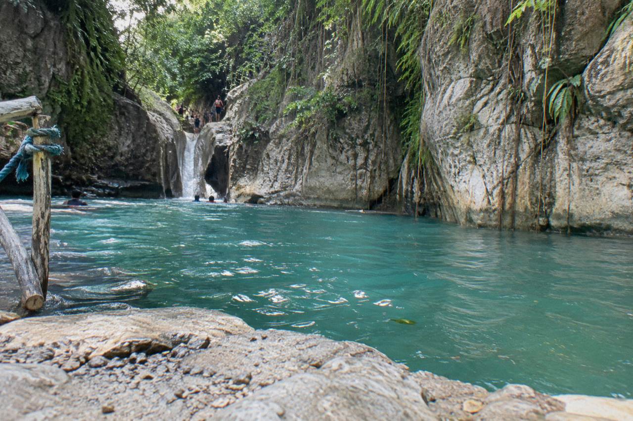Turquoise waterfall pool framed by rock walls in a tropical canyon