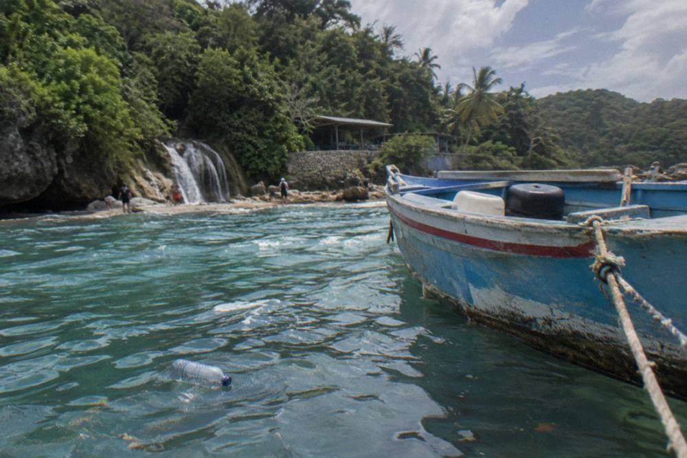 Wooden fishing boat anchored in clear shallow water beside a palm-lined beach