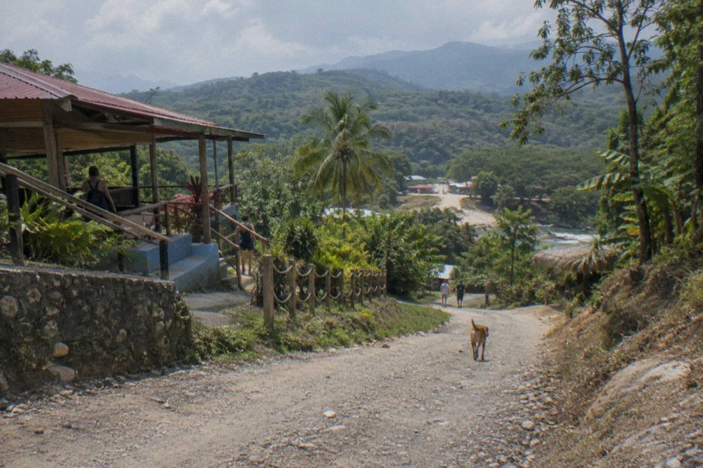 A rural road winding through green hills toward a small Dominican town in a valley