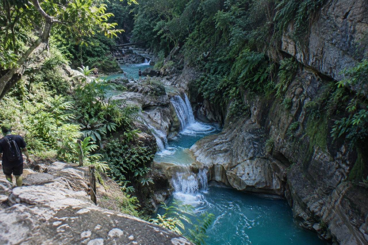 A narrow canyon of limestone rock with turquoise pools and small waterfalls flowing between steep forested walls