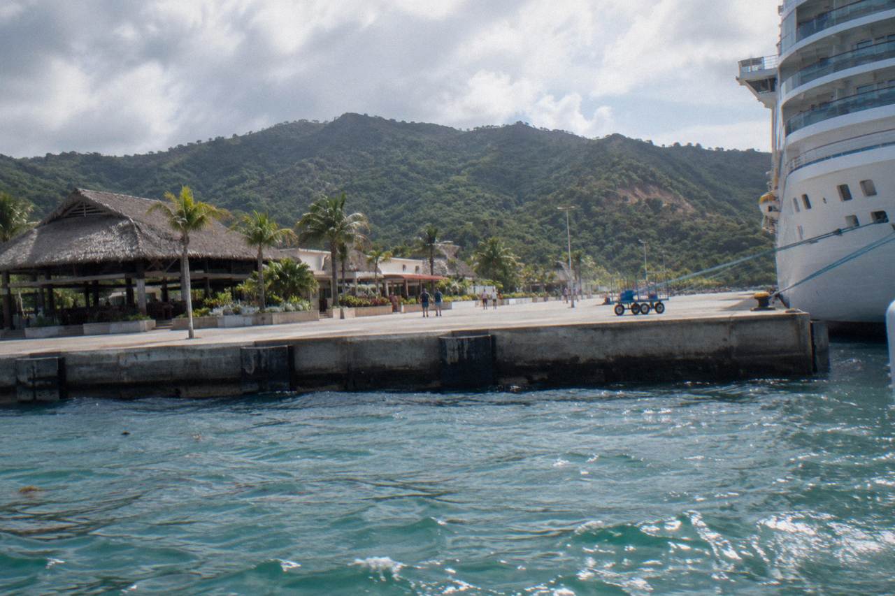 Cruise ship docked at a tropical port terminal with turquoise water and green hills