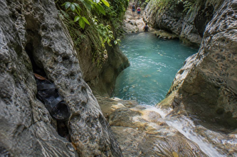 Turquoise waterfall pool in a narrow forested canyon with rock walls