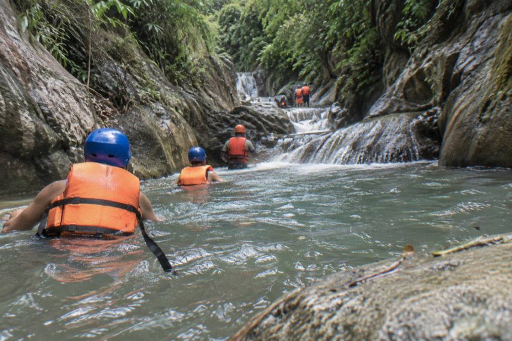 Group of visitors in helmets and life jackets wading through a canyon stream