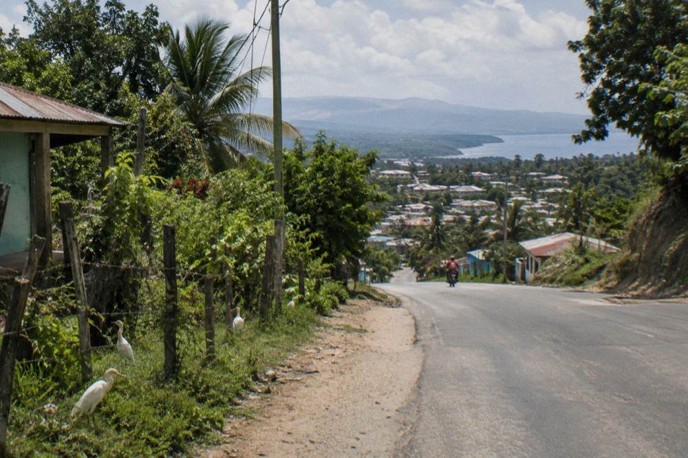 Winding rural road through green hills toward a small town in the Dominican countryside