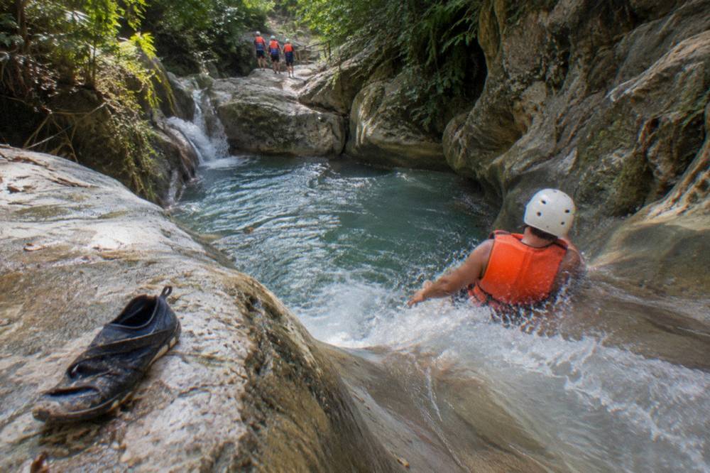 Visitors in safety gear sliding down a natural rock slide into a deep pool