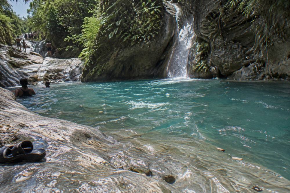 Clear turquoise waterfall pool surrounded by limestone rock and green forest
