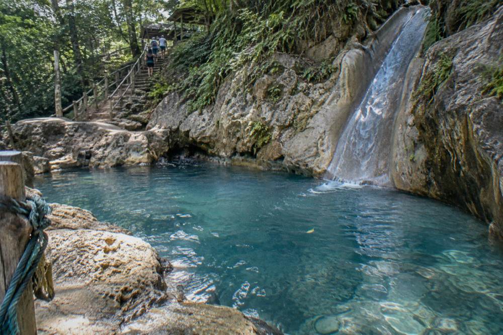 Morning sunlight on an empty blue pool below a rock slide at the waterfalls