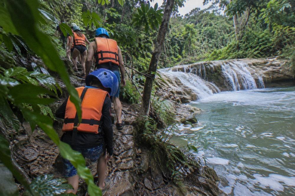 Family group in helmets and life jackets walking a jungle trail beside the river
