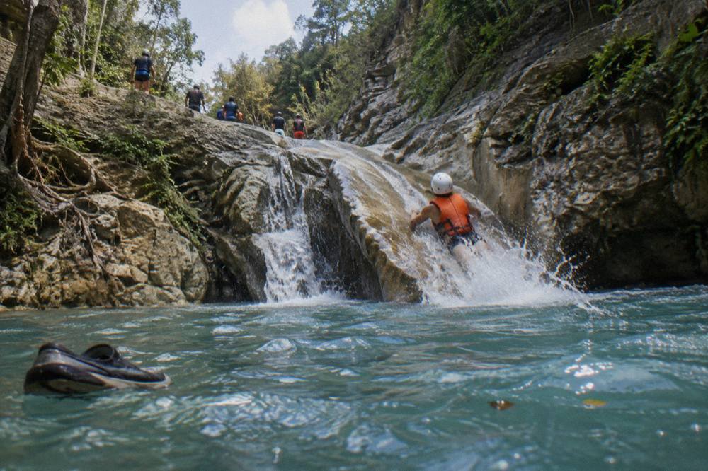 Swimmer in helmet and life jacket sliding down a smooth rock chute into a pool
