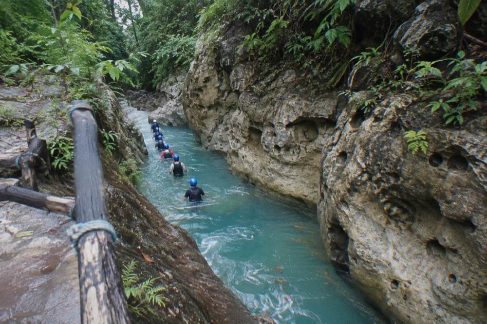 Guided group in helmets and life vests wading through a narrow turquoise canyon passage