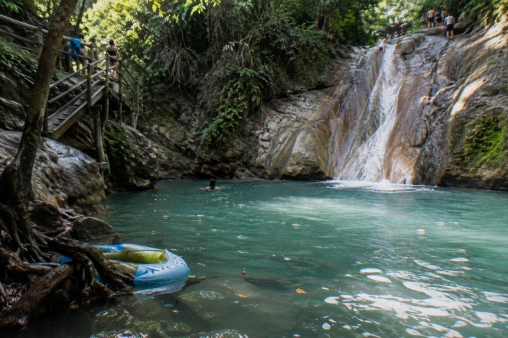 Waterfall pool at the base of a rock slide with forest canopy overhead at Damajagua