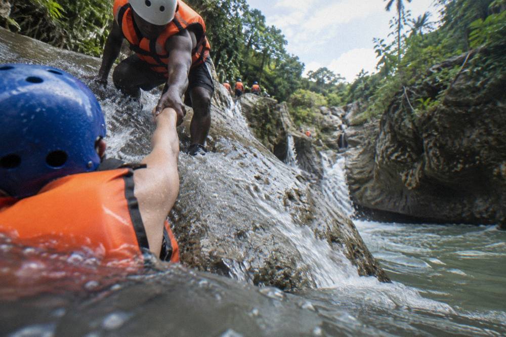 Guide in helmet and life jacket helping a visitor at the edge of a rock slide