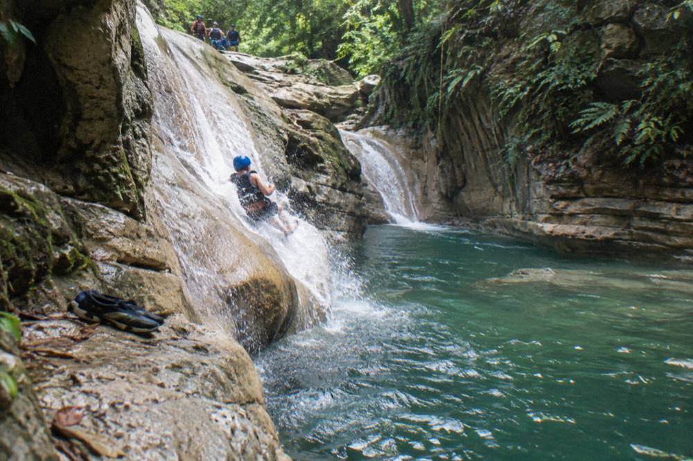 Person in helmet and life jacket sliding down a smooth rock chute into a deep pool