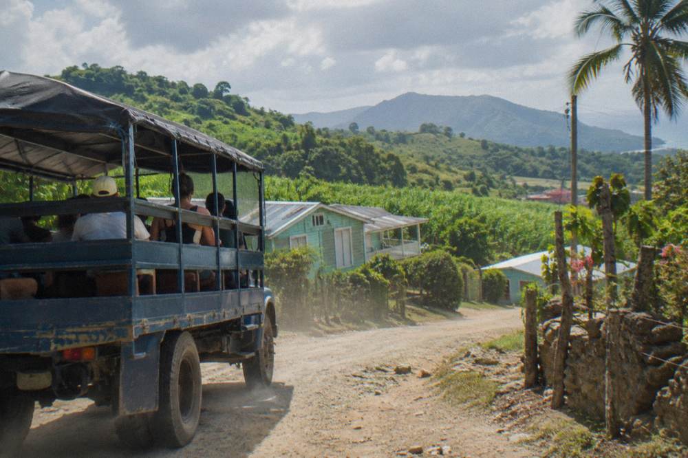 Open-sided tour vehicle on a dirt road through green hills near Puerto Plata