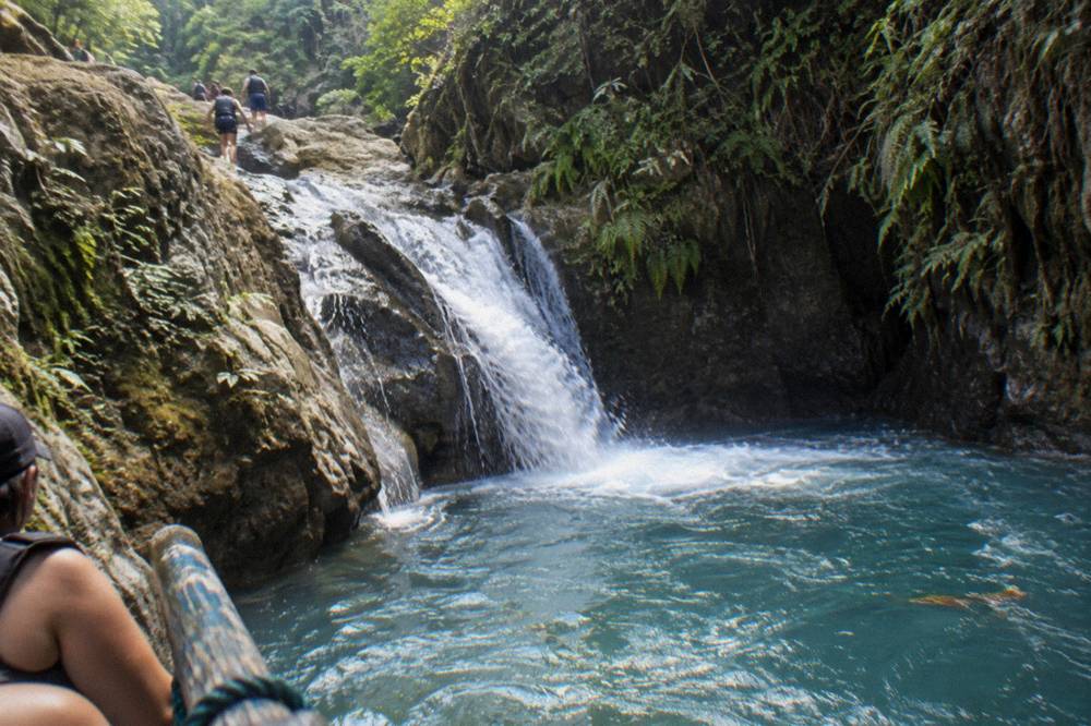 Waterfall cascading into a clear blue pool with forested canyon walls rising on both sides