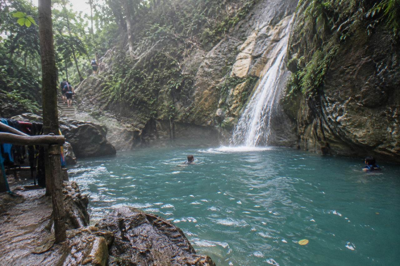 Turquoise waterfall pool in a forested canyon with rocky cliffs and cascading water