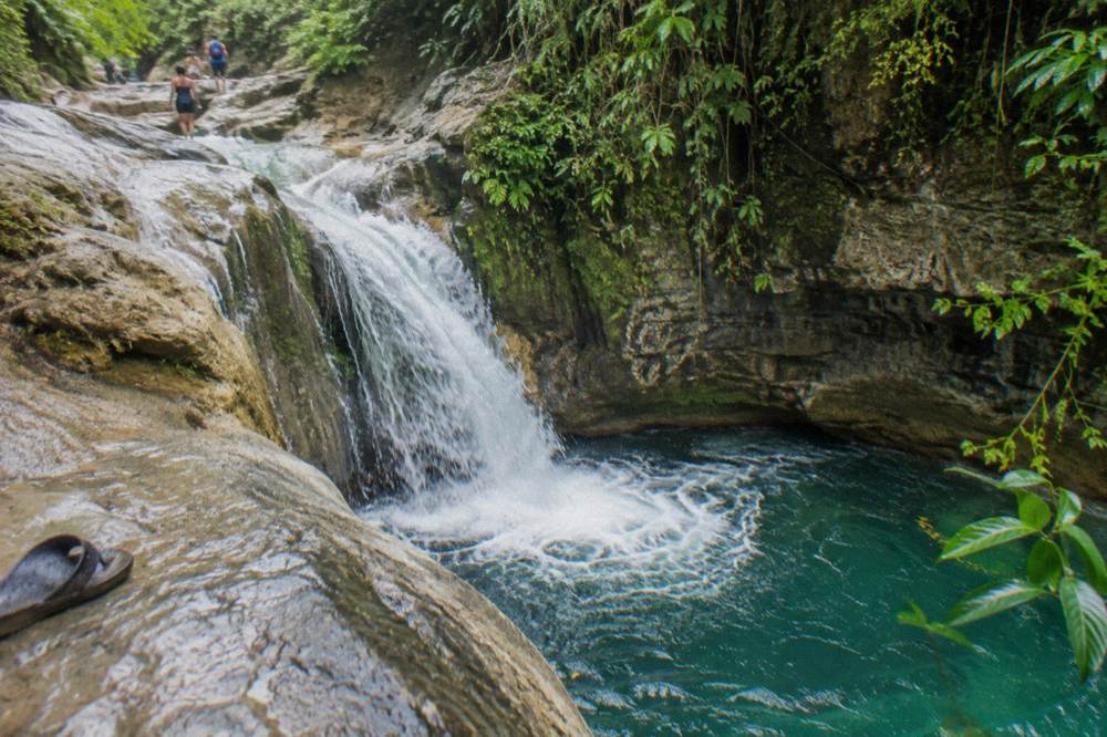 Waterfall pouring into a deep green pool surrounded by tropical foliage