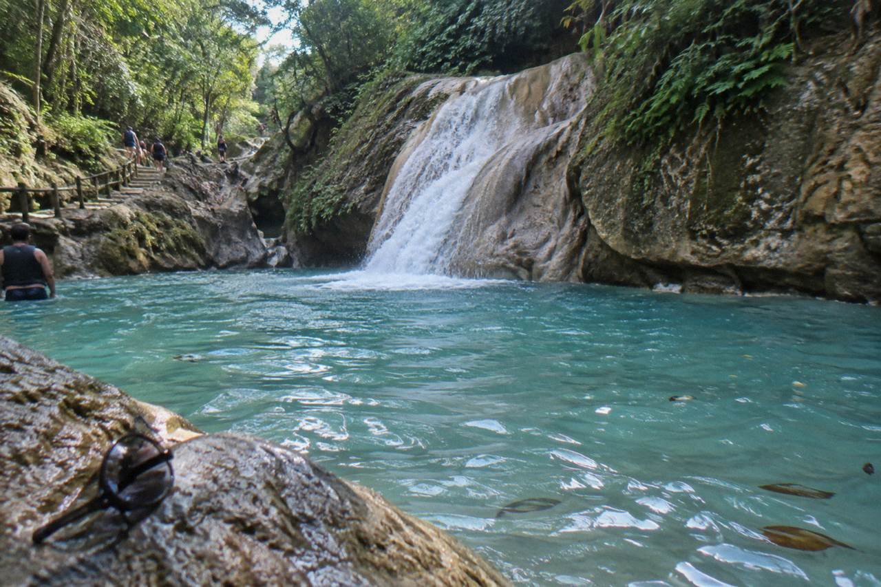 Turquoise waterfall pool in a narrow forested canyon with rocky walls