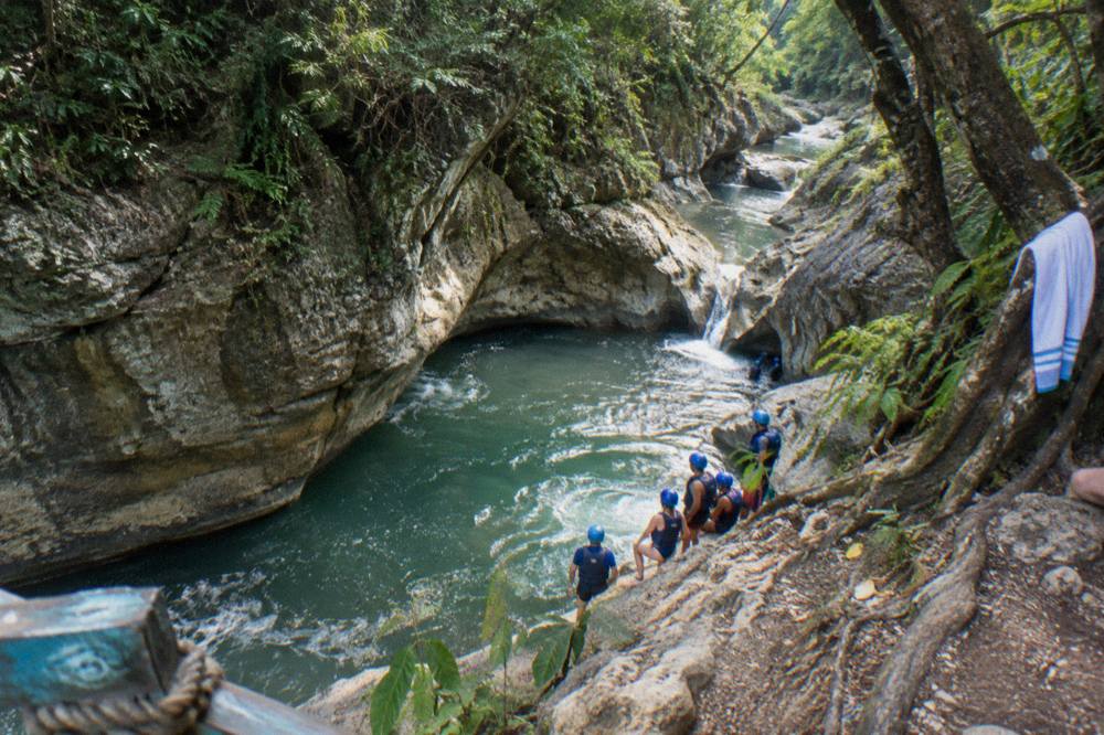 Canyon river winding between rock walls with a guide group in helmets waiting at the edge of a pool
