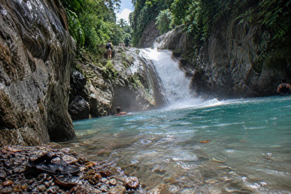 Waterfall cascading into a clear turquoise pool framed by canyon rock and tropical trees