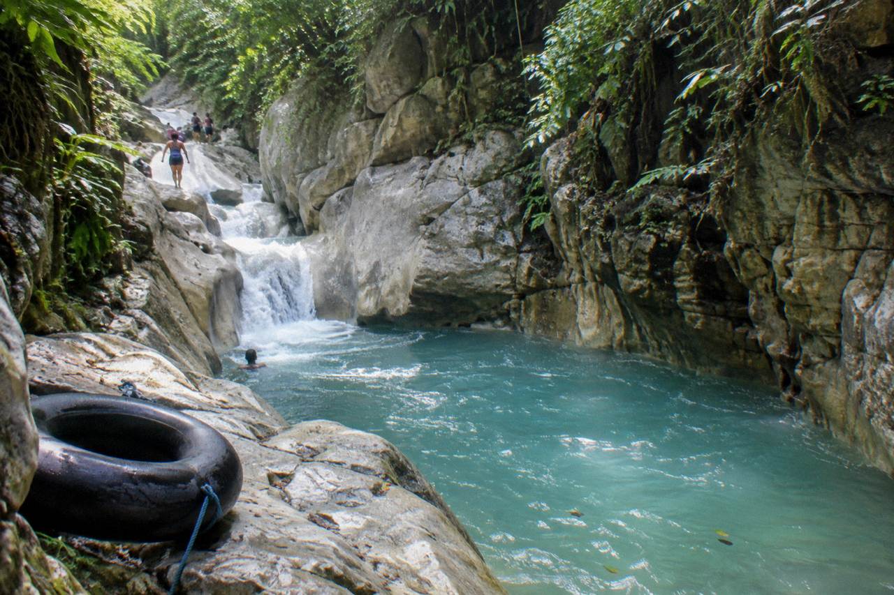 Turquoise waterfall pool in a narrow forest canyon with limestone walls