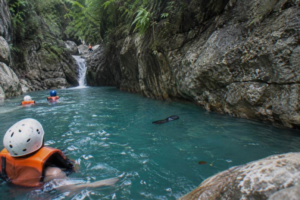 Visitors in helmets and life jackets floating in a deep turquoise canyon pool