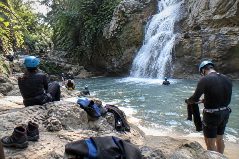 Group of hikers in helmets resting on rocks beside a wide cascade at the canyon exit