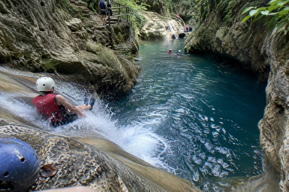 Swimmer in a helmet and life vest sliding into a deep blue pool between rock walls