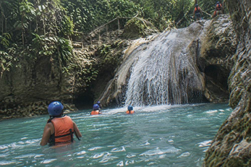 Group of visitors in helmets and life jackets wading through a clear turquoise pool
