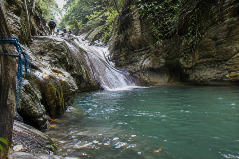 Calm turquoise pool at the base of a rock slide with morning light on the canyon walls