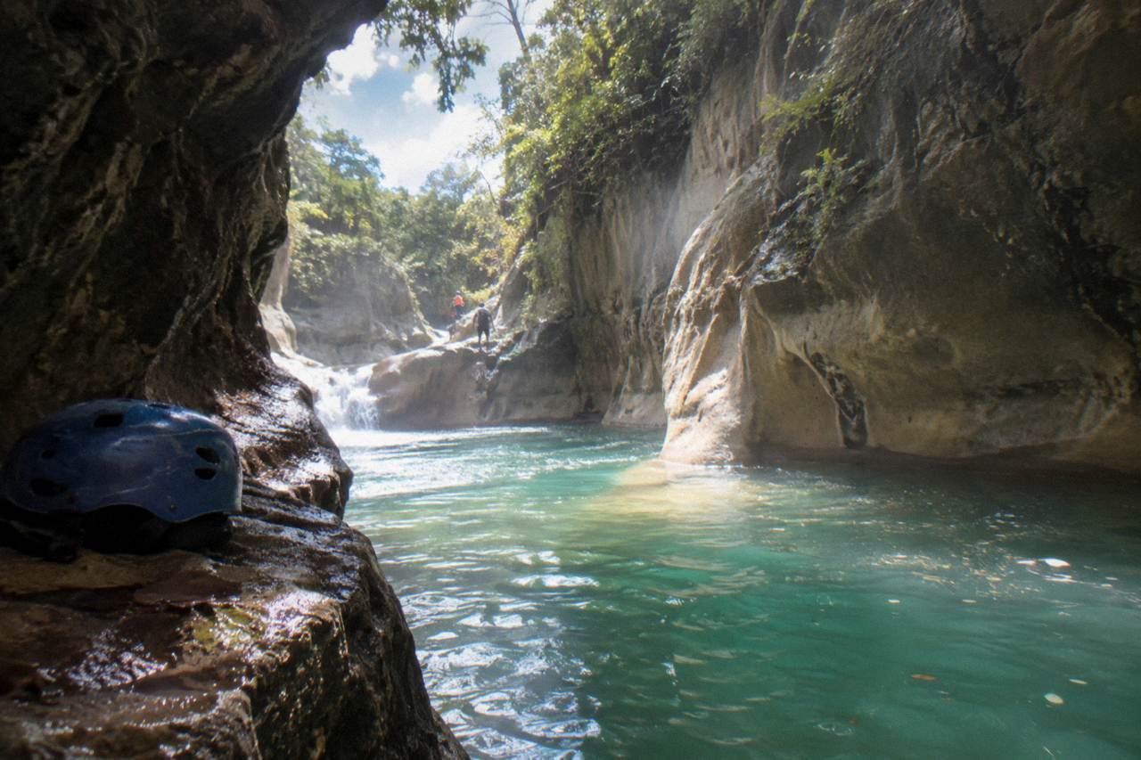 Turquoise waterfall pool framed by steep canyon walls in a tropical forest