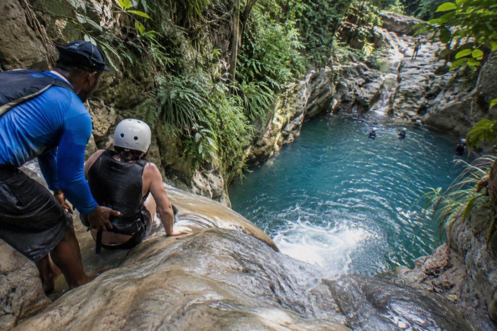 Waterfall pool with a guide and visitor preparing to slide into the water